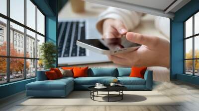 A close-up image of a woman using her smartphone at her office desk, checking messages. Wall mural