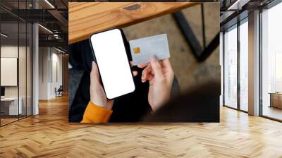 A close-up top view image of a woman sits at a table, holding a credit card and her smartphone. Wall mural