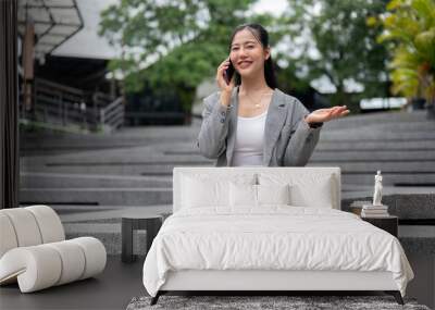 A confident Asian businesswoman is talking on the phone while sitting on the stairs outdoors. Wall mural