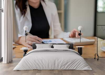 A cropped image of a businesswoman is reviewing business data report and using a calculator. Wall mural