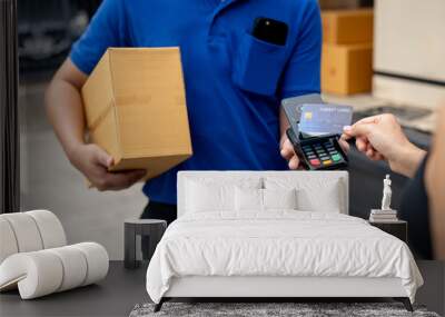 A customer tapping her credit card on a card reader before receiving a package from a delivery man. Wall mural