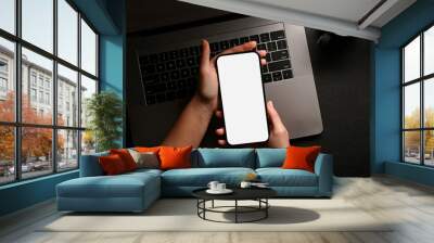 A female hands holding a smartphone white screen mockup over modern black office desk Wall mural