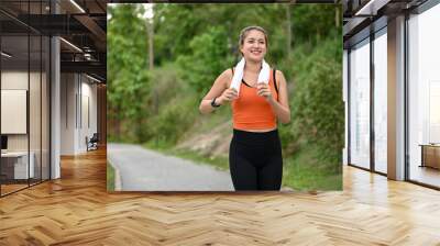 A happy Asian woman in sportswear enjoys running along the street in the nature park alone Wall mural