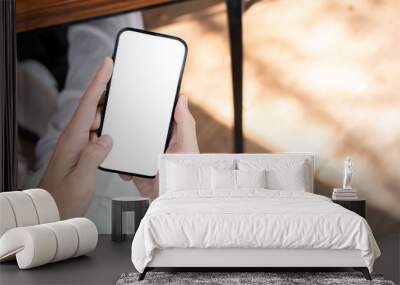 A man using his smartphone at a table in a cafe, with a white-screen smartphone mockup. Wall mural