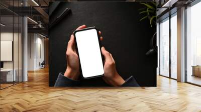 Above, A smartphone blank white screen mockup in a man's hands over black workspace. Wall mural