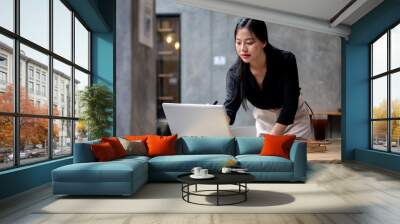 An attractive, confident Asian businesswoman is focusing on her work while leaning on her desk. Wall mural