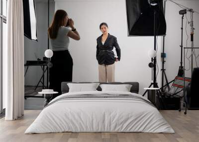 An attractive Asian female model is posing for a photographer in a modern fashion studio. Wall mural