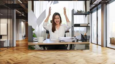 Angered, furious Asian businesswoman throwing up papers at her office desk. Wall mural