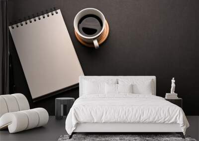 Black workspace table with a cup of coffee, an empty spiral notepad and copy space Wall mural