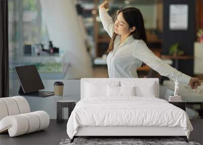 Businesswoman relaxing in office room, stretching her arms and back while sitting at workplace Wall mural