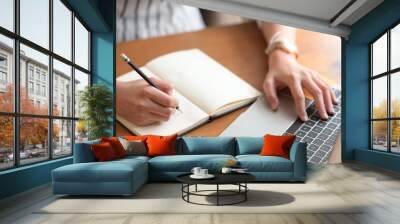 Businesswoman writing note while using laptop at table in office Wall mural