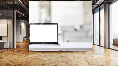 Cropped shot of simple workspace with blank screen laptop and coffee cup on white table with blurred office room Wall mural