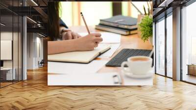 Cropped shot of woman freelancer writing on notebook on table in office Wall mural