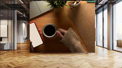 Female relaxing with mock up smartphone and drinking coffee on wooden worktable with supplies Wall mural