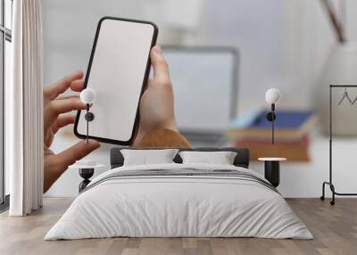 Female worker using mock-up smartphone in office room with laptop and supplies in blurred background Wall mural