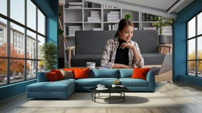 Happy Asian woman sits in her living room calculating taxes and managing household expenses. Wall mural