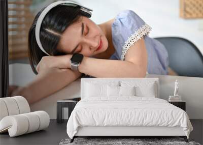 Relaxed young Asian female fall asleep at her desk while listening to music Wall mural