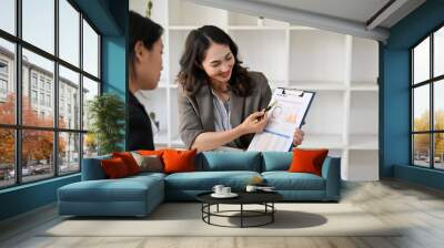 Smart Asian female accountant or financial analyst explaining financial data report to her colleague Wall mural