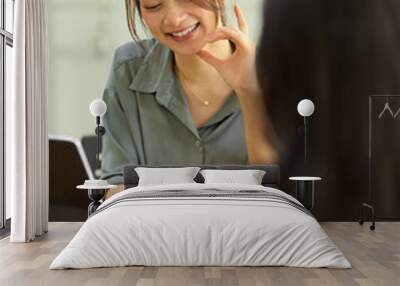 Smiling female workers talking with colleague and pointing on blank notebook Wall mural