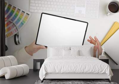 Top view of a female graphic designer holding a tablet mockup over her minimal white office desk. Wall mural