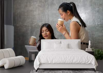 Two gorgeous Asian businesswomen are discussing work while enjoying coffee together in the office. Wall mural