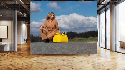 Elegant middle-aged woman in a fashionable pantsuit and with a yellow travel bag in hand on an empty track. Wall mural