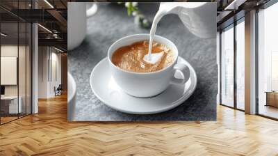 Pouring creamer into a cup of coffee on grey background Wall mural