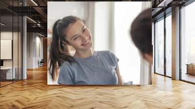 cute young teen girl with a smile on her face looks at herself in the mirror Wall mural