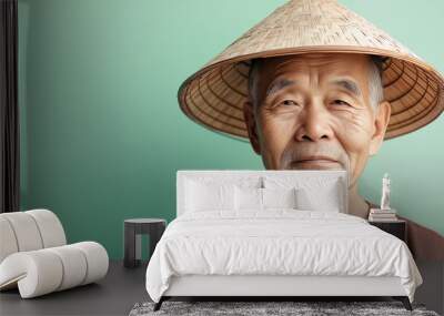 Elderly asian farmer posing in traditional conical hat and brown shirt against a green backdrop Wall mural