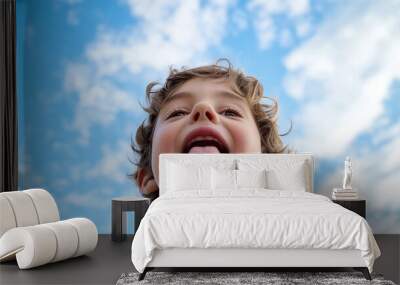 Joyful young boy playfully sticking his tongue out while enjoying a sunny day under a clear blue sky with fluffy white clouds Wall mural