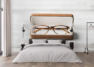 Pair of eyeglasses in a brown case placed on a light wooden surface. The image highlights eyewear storage and protection with a focus on the simple and elegant design of the glasses Wall mural