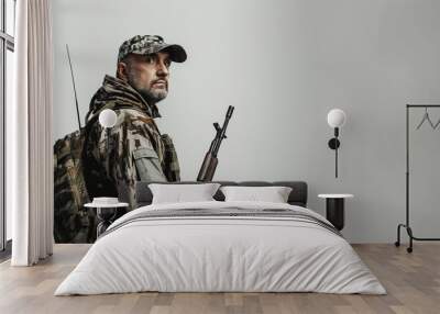 Portrait of serious soldier in camouflage, holding rifle, on gray background, prepared for mission, military concept Wall mural