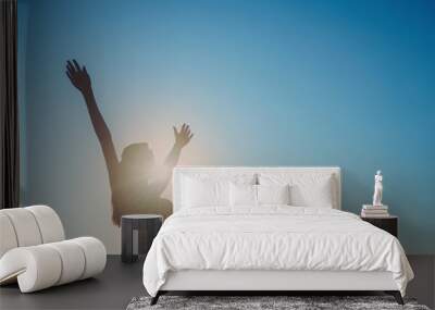 Silhouette of a girl with her hands wide apart, blue sky background Wall mural