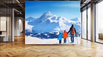 Ski tourist man with backpack with children wearing in colorful sport clothes standing in snowy mountain landscape, rear view Wall mural