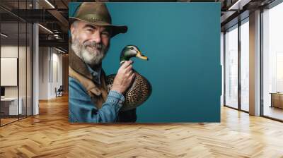 Smiling man in hat holding colorful duck against blue background, companionship, nature, wildlife concept Wall mural