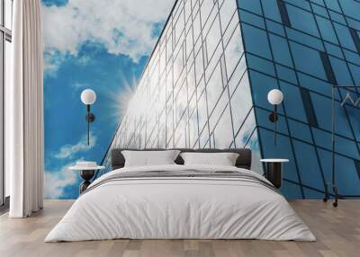 sunlight shines from behind office building with panoramic windows against blue sky with cumulus whi Wall mural