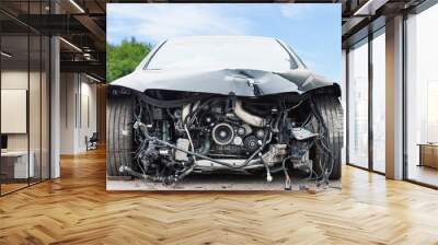 Front view of crashed car with damaged car parts against green bushes and blue sky, car crash accident on the street Wall mural