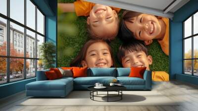 Four happy children lying on green grass, smiling and enjoying a sunny day. Wall mural