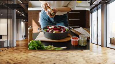 Close-up view of hands sprinkle pepper from manual spice mill on vegetables in a baking pan Wall mural