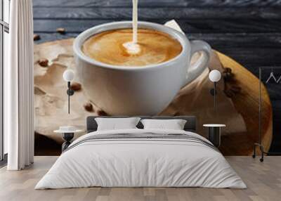 Pouring milk in coffee. Cup with cappuccino on wooden plate Wall mural