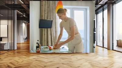 Young woman preparing a healthy meal in a modern kitchen during daylight hours Wall mural