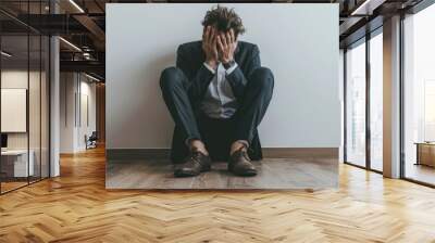 Businessman facing emotional struggle, Depressed professional sitting on floor with hands covering face against white wall Wall mural