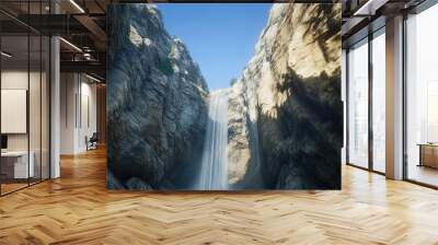 A serene waterfall flowing through a narrow gorge, with smooth rock walls on either side and a clear blue sky above. Wall mural