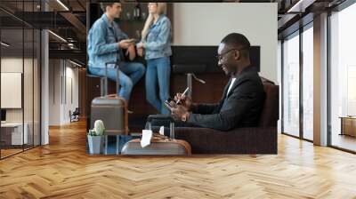 Businessman working on tablet PC while waiting for his flight at airport lounge. Wall mural