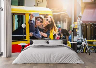 A couple of blogger tourists from Southeast Asia. Visit Phuket in Thailand are selfies on tuktuk. Captured in the old town of Phuket during write travel reviews with sunlight in travel concept . Wall mural