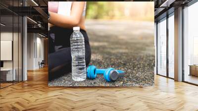 Women are sitting tired of their workouts, with water bottles and headphones on the side at the park with green leaves blur bokeh background in sport and healthy concept with copy space. Wall mural