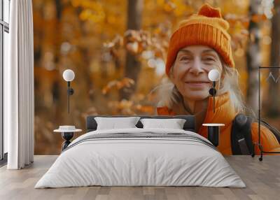 A smiling woman in an orange jacket and hat stands in a vibrant autumn forest. Wall mural