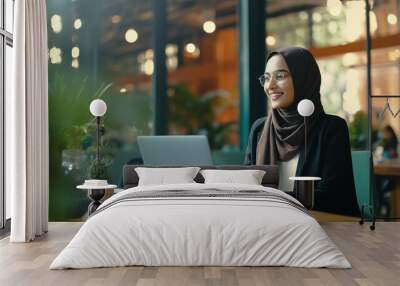 Middle Eastern Muslim woman wearing a hijab working on a laptop in a modern office or cafe on a video call Wall mural