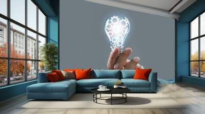 A hand holding a glowing light bulb with gears inside, symbolizing innovation and creativity in technology and ideas. Wall mural