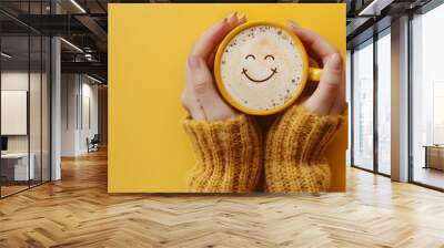 Closeup woman hands holding coffee cup with smile face drawn on coffee isolated on yellow background Wall mural